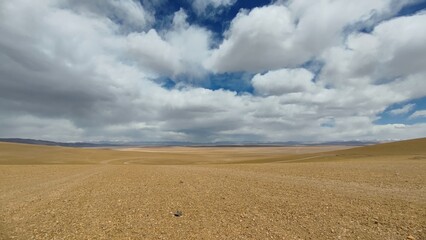 Fototapeta na wymiar Blue sky and clouds above a yellow desert in Tibet 