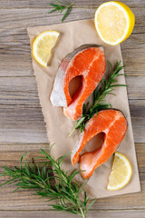 Steak of fresh raw red fish salmon with lemon, rosemary and pepper on wooden background