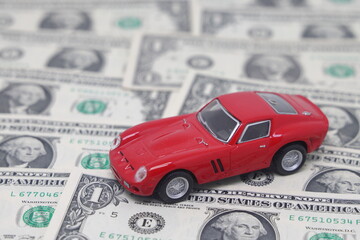 Small toy car on dollar banknotes in the form of a road, isolated on a white background, the cost of owning a car.