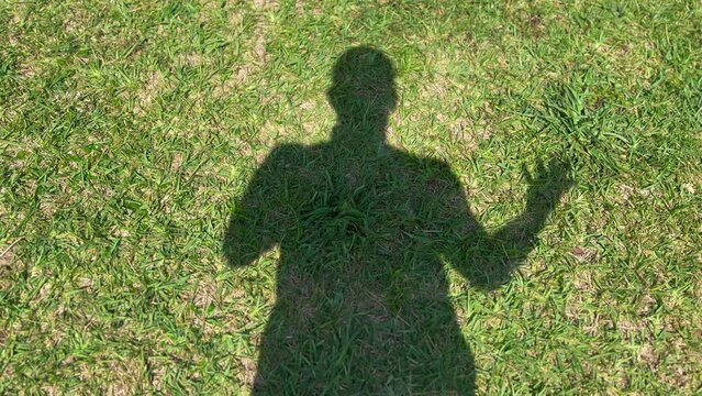 Silhouette shadow of man standing in green grass moving arm around on sunny day