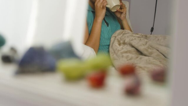 South Asian Woman Drinking Tea In Bed, Crystals Blurry In Foreground.