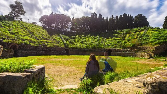 Young tourists enjoy the view of the ancient, overgrown ruins of a Roman or Greek amphitheater - time lapse