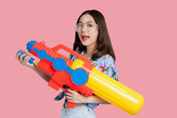 Beautiful Asian woman holding a plastic water gun and isolated on pastel pink background in the studio. She was ready for the Songkran Festival in Thailand.