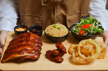 Grilled pork bbq ribs served with cherry tomatoes. basil and barbeque sauce on wooden cutting board over dark background. Close up