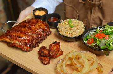 Grilled pork bbq ribs served with cherry tomatoes. basil and barbeque sauce on wooden cutting board over dark background. Close up
