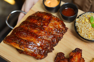 Grilled pork bbq ribs served with cherry tomatoes. basil and barbeque sauce on wooden cutting board over dark background. Close up