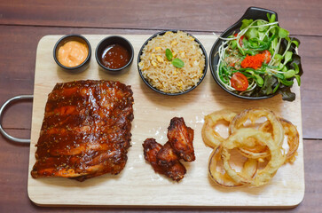 Grilled pork bbq ribs served with cherry tomatoes. basil and barbeque sauce on wooden cutting board over dark background. Close up