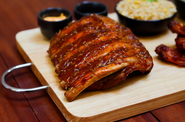 Grilled pork bbq ribs served with cherry tomatoes. basil and barbeque sauce on wooden cutting board over dark background. Close up