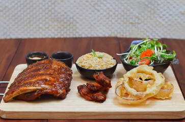 Grilled pork bbq ribs served with cherry tomatoes. basil and barbeque sauce on wooden cutting board over dark background. Close up