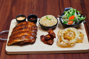 Grilled pork bbq ribs served with cherry tomatoes. basil and barbeque sauce on wooden cutting board over dark background. Close up