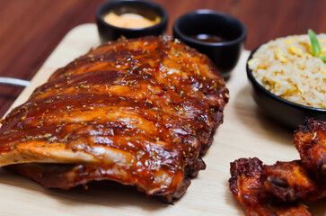 Grilled pork bbq ribs served with cherry tomatoes. basil and barbeque sauce on wooden cutting board over dark background. Close up