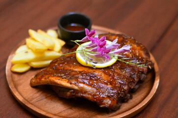 Grilled pork bbq ribs served with cherry tomatoes. basil and barbeque sauce on wooden cutting board over dark background. Close up