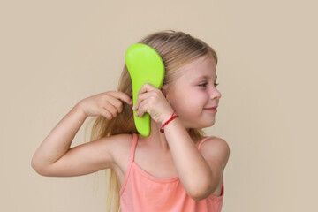 Candid portrait of cute little girl combing her long hair with detangler brush	