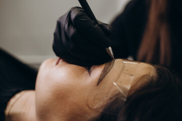 Beautician hand doing brow permanent makeup on an attractive female face