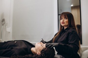 Beautician hand doing brow permanent makeup on an attractive female face