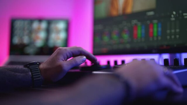 Close-up of a man's hand making edits on a special panel. Young man in glasses working on video editing on computer doing montage and color correction. Concept of creating video content.