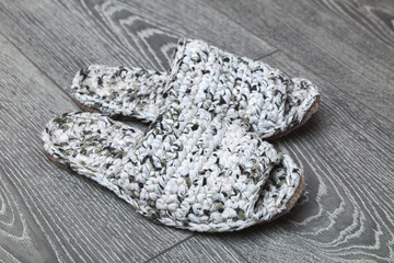 White knitted handmade slippers stand on a gray floor