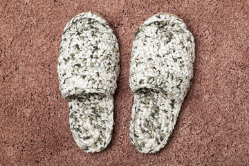 White knitted handmade slippers stand on a red carpet