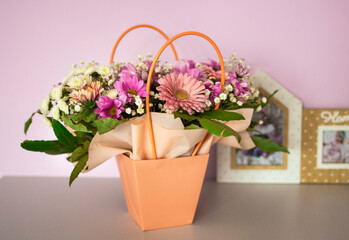 A composition of flowers in a festive box stands on the bedside table near a frame with a children's photo. A gift for a beloved woman