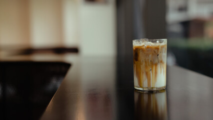 A glass of iced coffee sits on a table in front of a bar.