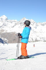Fototapeta na wymiar Skier in blue jacket, black helmet and orange pants on the piste slope in winter with snow mountains in Alps, Europe