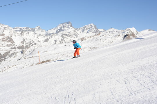Skier in blue jacket, black helmet and orange pants on the piste slope in winter with snow mountains in Alps, Europe