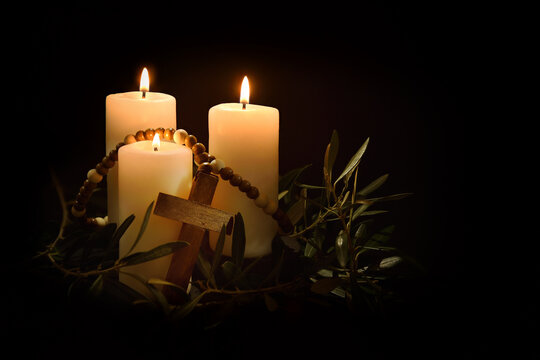 Candles illuminating cross and olive branches in the twilight
