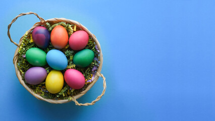 Basket with easter colored eggs on a blue background with a place for a text