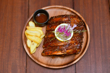 Grilled pork bbq ribs served with cherry tomatoes. basil and barbeque sauce on wooden cutting board on wood board.