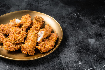 Breaded chicken strips, breast fillet meat on a plate. Black backgrund. Top view. Copy space