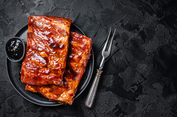 Ready for BBQ raw pork spare ribs with barbecue sauce. Black background. Top view. Copy space