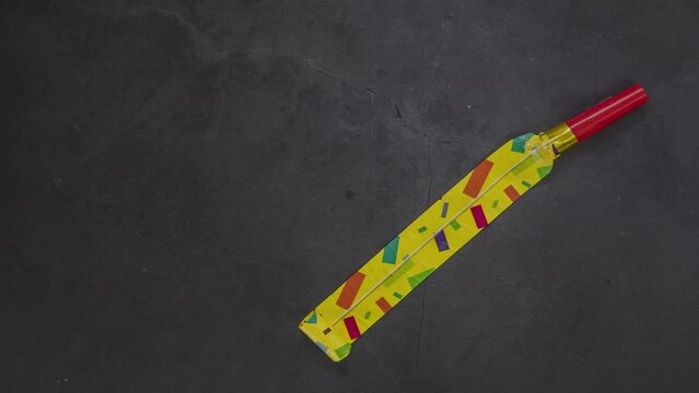 Birthday party blowouts whistles Rolled festive noisemaker or party whistle on concrete dark background, blowing in whistle top view in and out loop 4k Happy Birthday copy space