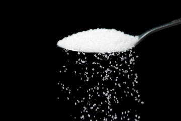 Macro photography of a teaspoon with white sugar on a black background, copy space. White sugar is...