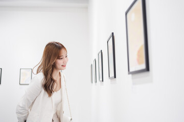 Woman visiting art gallery her looking pictures on wall watching photo frame painting at artwork...