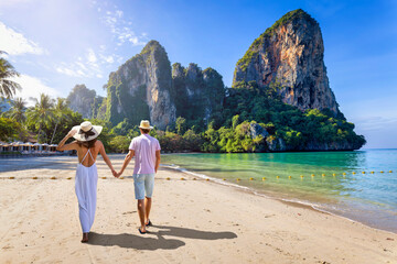 A happy couple on holidays walks down the empty Railay Beach at Krabi, Thailand, with emerald sea...