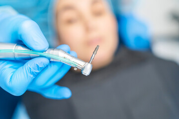 Closeup photo of dental implant in dentist hands with female patient in dental chair behind.