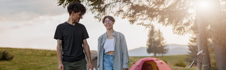 Obraz premium Happy cheerful couple carrying portative fridge at camping site. Vacation in mountains.
