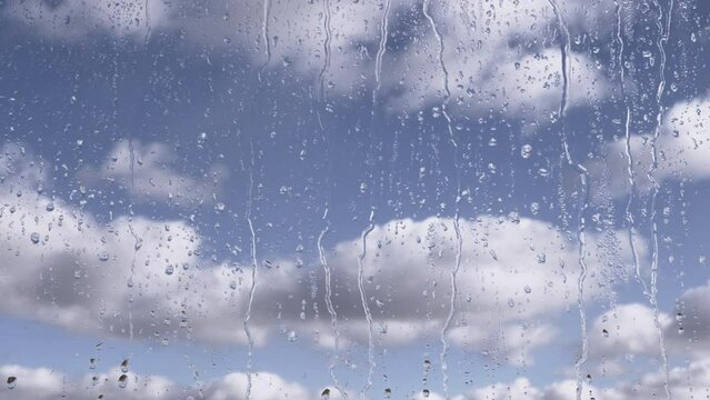 Rain Drops Flow Down Glass Against a Background of Moving Clouds and Grey Sky. Time-lapse. Fast-moving cumulus clouds. Rainy weather. Streams of water flow down the window on the glass. Meteorology.