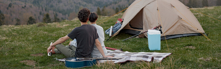 Back view on Caucasian couple of travelers sitting at tent and watching mountains landscape.