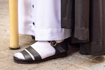 Detail of the foot of a nazareno or penitent wearing a black sandal and a white sock, doing his...