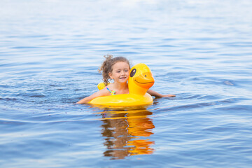 little cute  curly girl swimming in water, sea, river, lake with duck circle. happy child learning to swim. summer and vacation concept