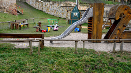 crawling wooden attraction on the sandpit. children have a stainless steel slide and rope nets for climbing and for greater safety on the bridge. stone sandstone wall in the background of kindergarten - obrazy, fototapety, plakaty