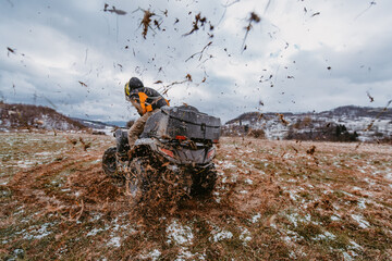 A man drives an ATV in the mud. Drift driving an ATV quad in mud and snow - obrazy, fototapety, plakaty