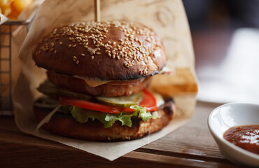 Juicy cheeseburger served on wooden plate. Big fat burger with melted cheese and fresh vegetables
