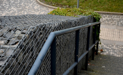 construction of a steep staircase by the stone wall car park with high durability even under heavy load galvanized steel floor grate and railings. gabion above him a wire fence. corridor, narrow
