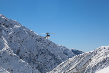 Naklejka na ściany i meble Helicopter flying in snow covered valley of Mountain in Himalaya. White helicopter on a white landscape with clear blue sky background. 