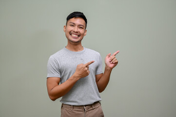 Cheerful Asian man pointing his fingers up at empty space, standing against an isolated background