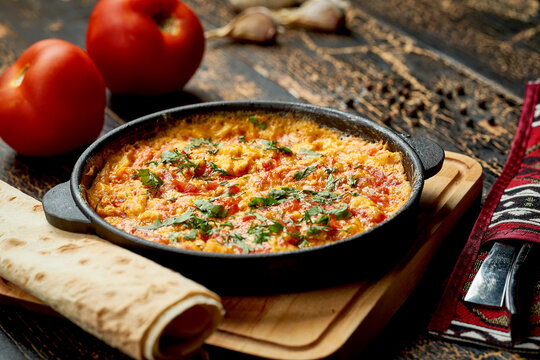 Menemen with eggs, tomato, green peppers, and spices served with bread in pan. Turkish breakfast