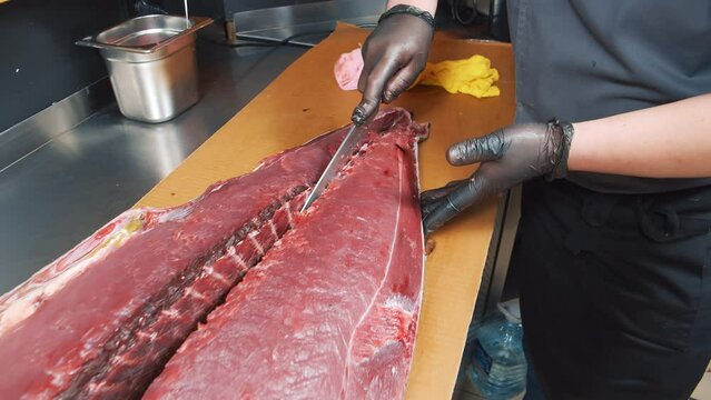 Close-up of the process of cutting tuna fish at the market. Male hands in gloves cutting a large fish with a knife.