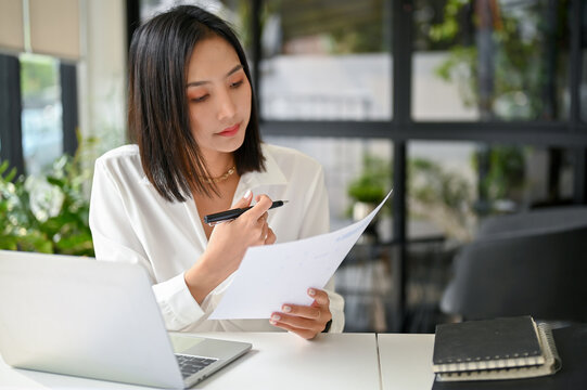 Focused Asian businesswoman reviewing business document or analyzing financial data report